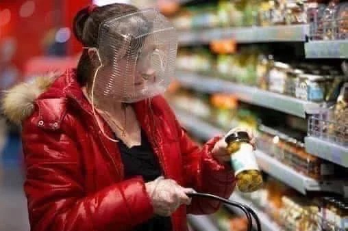 Woman shopping for olives while wearing a plastic deli container over her face.